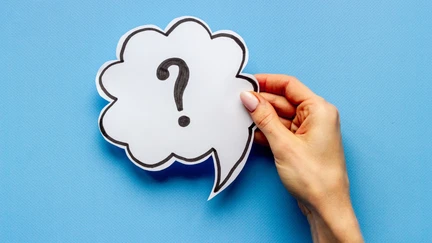 Photo of a hand holding a thought bubble with a question mark on a blue background.