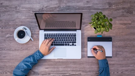 Photo of a person's hands writing notes next to a laptop.