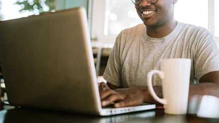 Photo of a person smiling at a laptop.