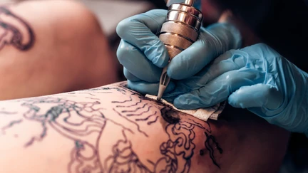 Photo of someone tattooing a person's limb.