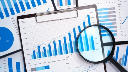 Clipboard with printouts of bar graphs and charts and a magnifying glass