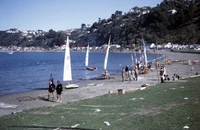 A group of people on the beach at Worser Bay preparing to take their small sailboats out on the water.