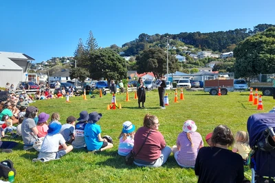 A crowd of families sitting on the grass in the sun watching a librarian with a microphone read Llama llama mad at mama.