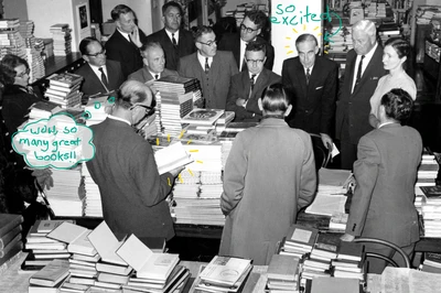 Black and white photo from 1963 of librarians standing around a table of books. Written on captions say 'so excited!' and 'wow, so many great books!'