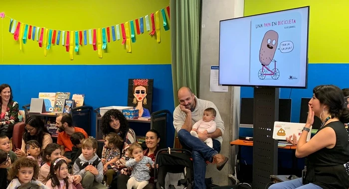 A librarian reads a book in Spanish to a large group of children and parents. A