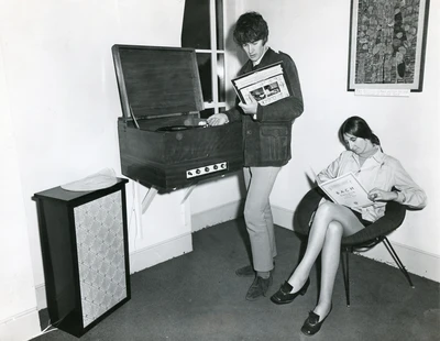 Black and white photograph of two people listening to music with a gramophone record.