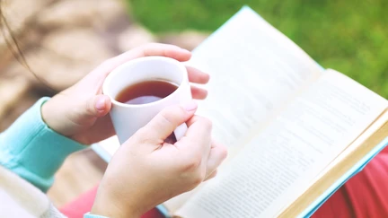 Person sitting outside with a book and a cup of tea