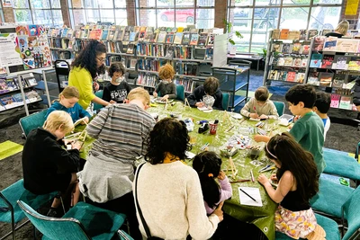 A table in the library surrounded by seated children painting on tiny canvases