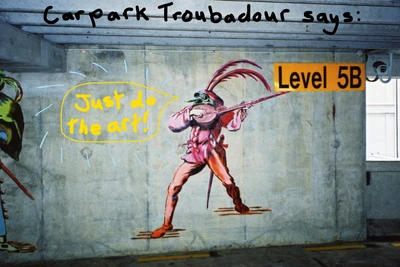 Carpark mural: troubadour dressed in red holding a lute with a green insect-like head. Edited text says: Carpark troubadour says Just do the art!