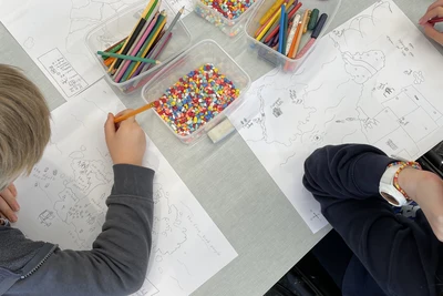 Looking down from above, four children around a small table working on their fantasy maps.