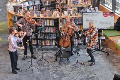 two violins, one cello, one viola in the New Zealand String Quartet performing in front of the Young Adult shelving at Johnsonville Library.