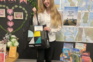 A smiling teen with long blonde hair holds up a large library bag