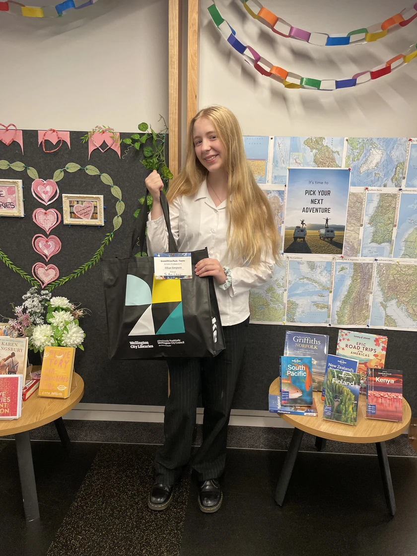 A smiling teen with long blonde hair holds up a large library bag