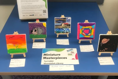 Five tiny canvases on easels displayed next to a sign saying Miniature masterpieces.