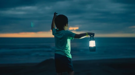 Boy with a lantern in the twilight looking out to sea