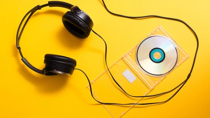 Headphones and a music cd on a vibrant yellow background.