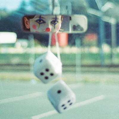 Photo on dice in a car window, a person in clown makeup looking through the rear-view mirror.