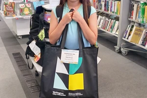 A smiling girl holds a large library tote bag full of prizes up to her chest