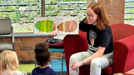 A librarian reads a book in te reo Māori to a group of entranced children.