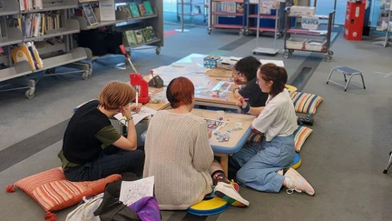 Four young people sit on colourful cushions around a low table, making badges
