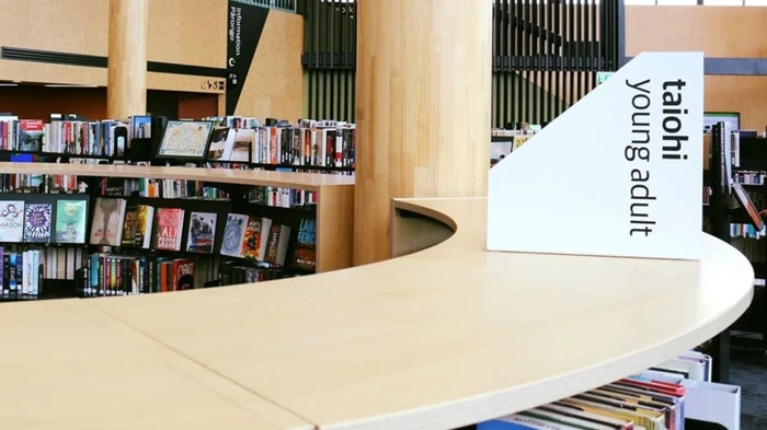 Library signage " Taiohi Young Adult" resting on top of a curved library shelvin