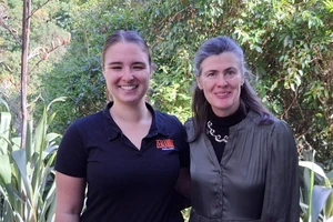 Two women in black Zealandia shirts stand in front of a background of native bush