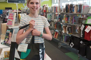 A girl in a stripy shirt grins while holding a large library bag full of books