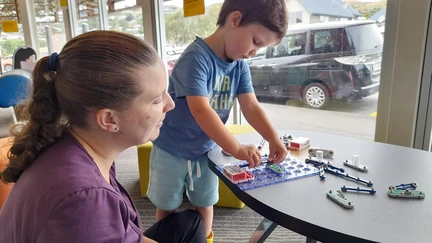 A young child tinkers with an electrical circuit while his caregiver looks on.