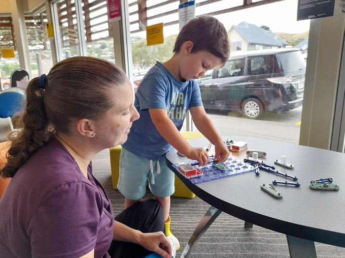 A young child tinkers with an electrical circuit while his caregiver looks on.