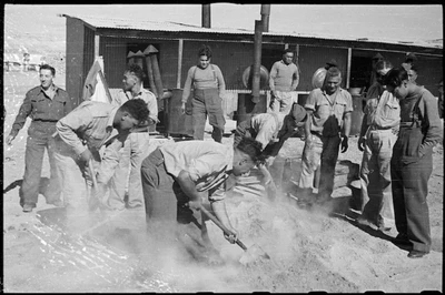 Two men from the Maori Battalion digging up a hangi of pork and potatoes for Christmas Dinner at the Maori Training Depot, Maadi.