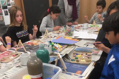 Children around a table using cardboard palettes begin painting.