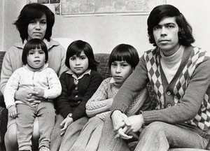 A black and white photo of a family of five, mother, three children, and father, sitting on a sofa.