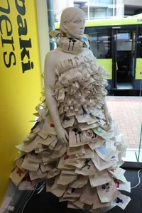 A mannequin in the library window wearing a long dress made out of pages of books.