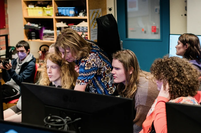 A group of rangatahi are clustered around a computer as a tutor shows them somet